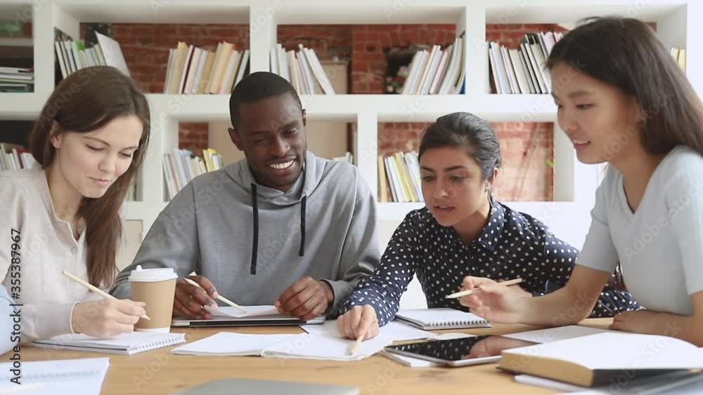 Multiracial college university students group study together prepare project make notes, happy diverse young people team write essay summary learn in teamwork do creative research homework in library