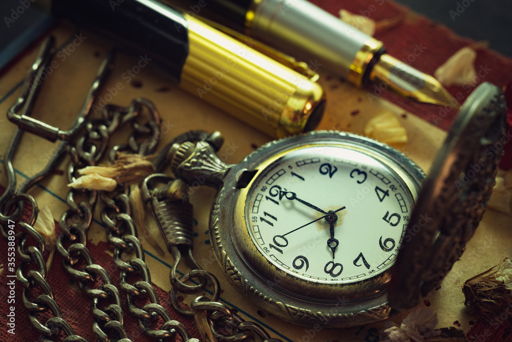 Fototapeta premium Vintage pocket watch and brass pen on old book. At 8 o'clock in morning. Education and vintage style concept.
