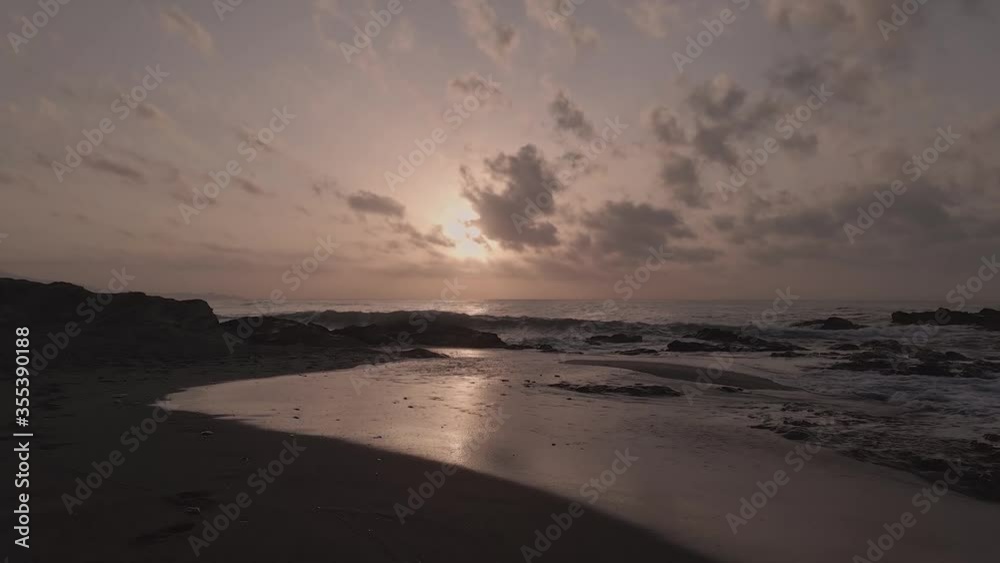 Aerial view low flying rocky sandy sunset beach with dramatic cloudscape horizon Aerial view low flying rocky sandy sunset beach with dramatic cloudscape horizon