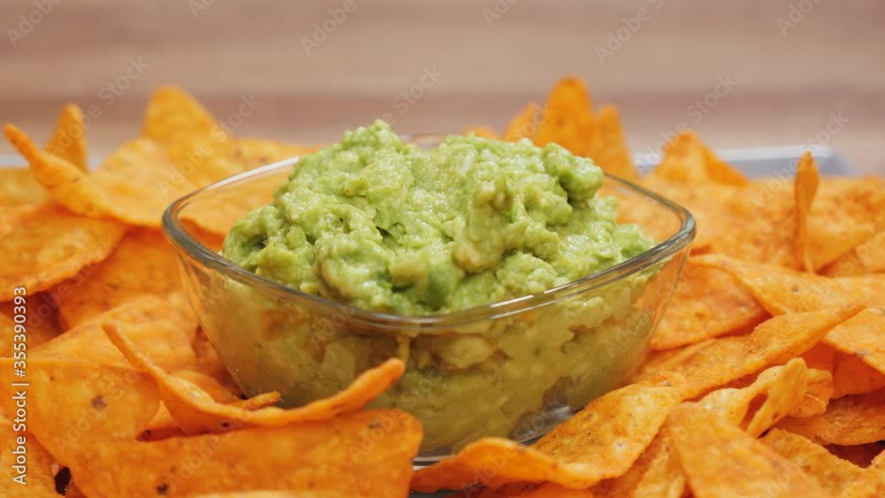 Hand taking delicious tortilla chip from a plate with guacamole in the center bowl - camera orbit around Hand taking delicious tortilla chip from a plate with guacamole in the center bowl - camera orbit around