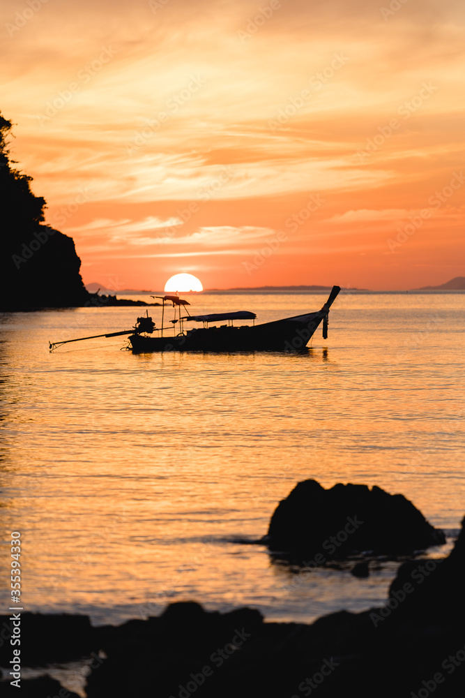 Sonnenuntergang in Thailand mit Longtailboot und Wolken und Felsen im Meer
