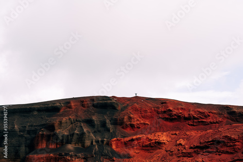 Martian landscapes in Iceland. The red crater of The Seydisholar volcano. The quarry of red soil mining. Silhouette of a man on top of a red-black mountain.