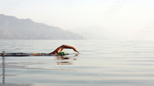 Unknown triathlon swimmer at sea. athletic young woman swimming freestyle in morning open water