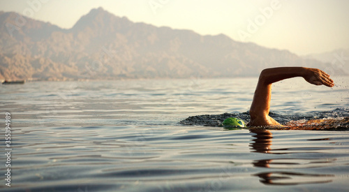 Unknown triathlon swimmer at sea. athletic young woman swimming freestyle in morning open water
