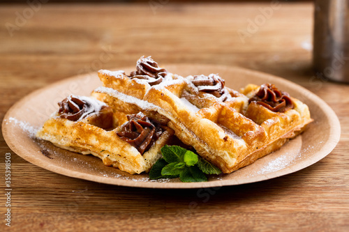 .Viennese waffles on a disposable plate with peanut butter, icing sugar and mint.