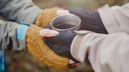 Male and female hands hold tea in a mug from a thermos on a background of nature