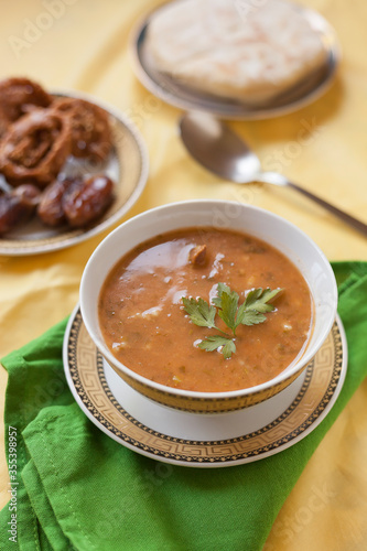 Vertical shot of a bowl of harira, a traditional Moroccan soup dish served hot typical of Ramadan breakfasts accompanied by dates and chebakia sweets on a table set with copy space. photo