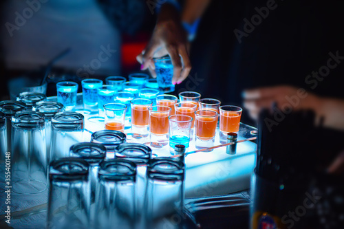 Variation of hard alcoholic shots served on bar counter, Blue and Orange alcohol shots in club with blurred girl taking shot