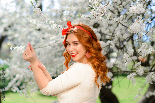 Portrait of beautiful red-haired young woman in white dress in spring flowers, blossom