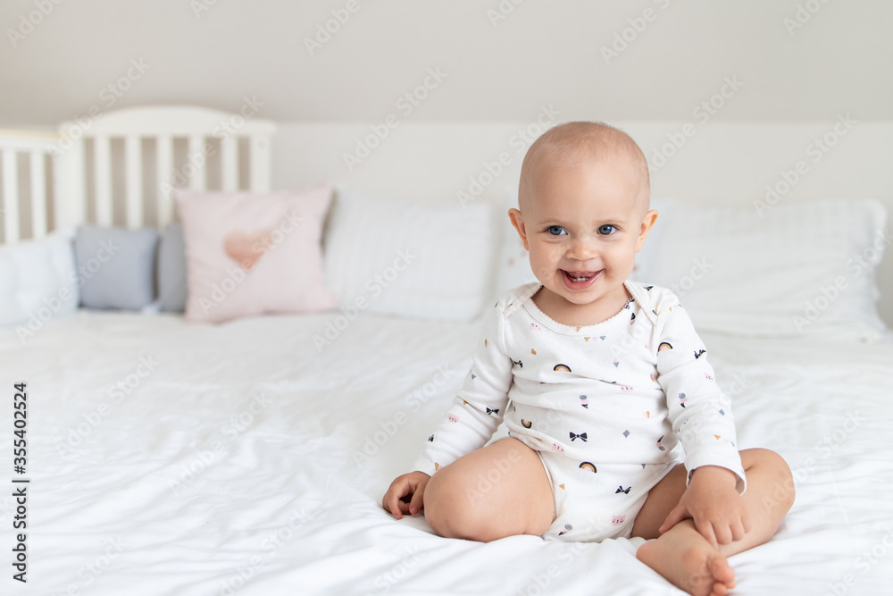 Cute baby girl on a white bed sits and smiles