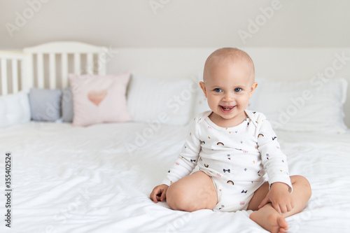 Cute baby girl on a white bed sits and smiles