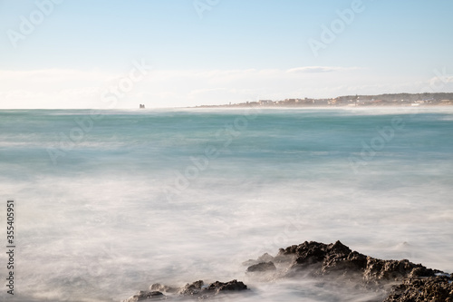 Mare Jonio moved, Puglia, South Italy, the waves agitated by the wind of Scirocco foam approaching the shore creating a haze effect, in the background is visible the coast of Salentina and old tower.