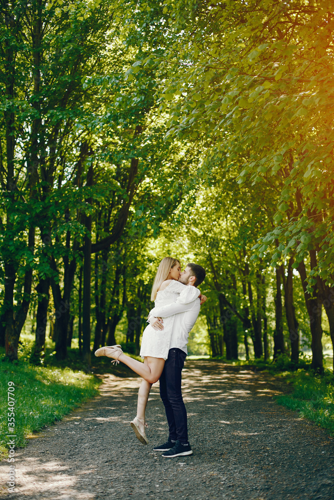 A beautiful and gentle girl with light hair and a white dress is walking in a sunny summer forest with her handsome guy in a white shirt and dark pants A beautiful and gentle girl with light hair and a white dress is walking in a sunny summer forest with her handsome guy in a white shirt and dark pants