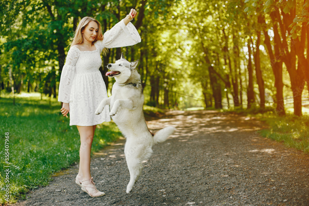 Beautiful and gentle girl with light hair dressed in white dress is playing along with her sweet doggy in summer green park. Beautiful and gentle girl with light hair dressed in white dress is playing along with her sweet doggy in summer green park.