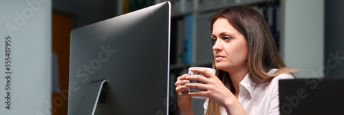 Fototapeta Naklejka Na Ścianę i Meble -  Woman holds mug and looks at monitor intensely