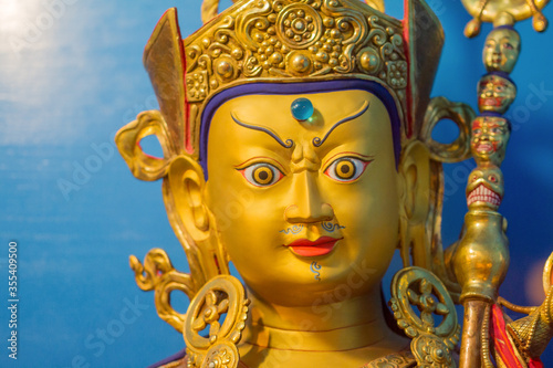 Gold statue of tibetan buddhist master Guru Rimpoche or Padmasambhava with blue background.