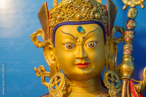 Gold statue of tibetan buddhist master Guru Rimpoche or Padmasambhava with blue background.