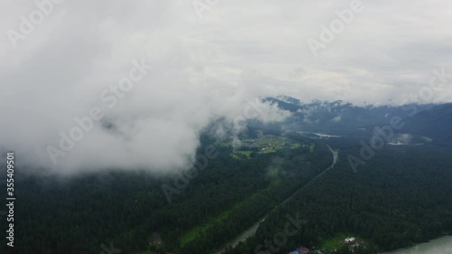 Aerial view. Flying sideways. Flying over green grassy rocky hills. Through the clouds. Through the mist. Altai Mountains, Siberia, Russia. Summer 2020