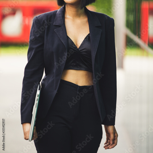 Young businesswoman walking and holding laptop on  blur urban background. 