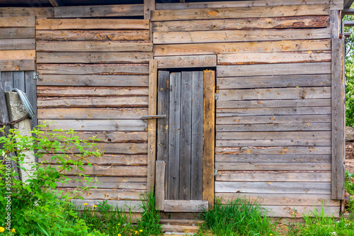 Wooden door in wall of old ugly barn from rough boards in summer