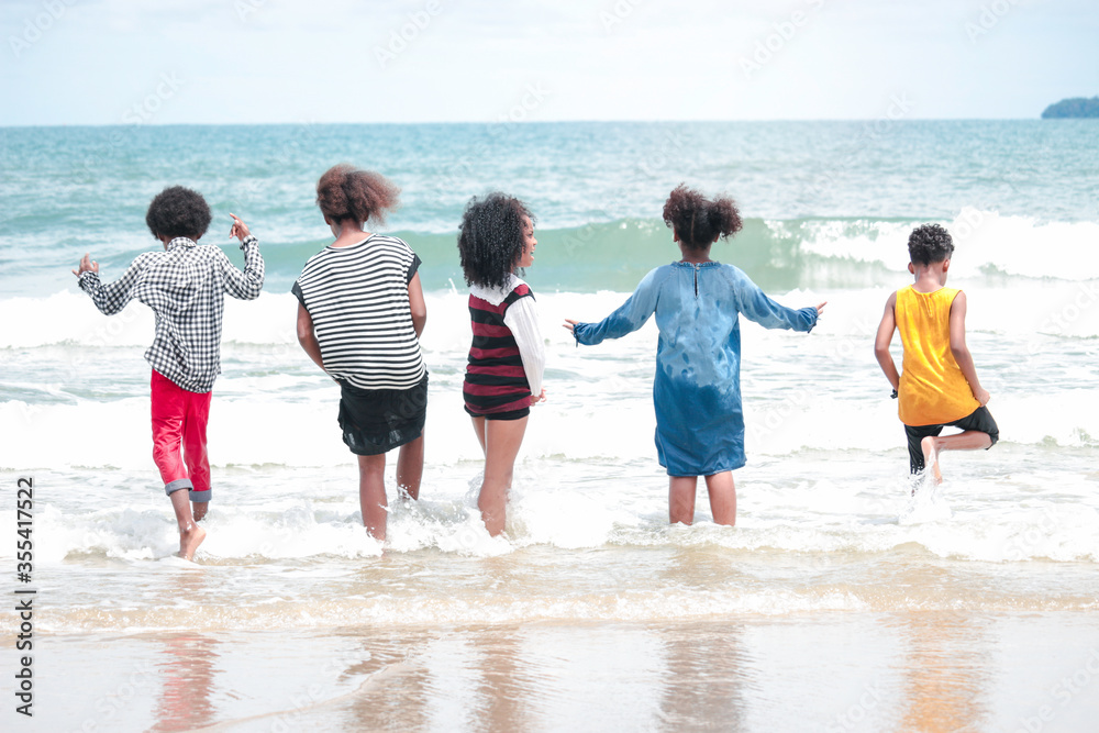 Group of boys and girls running and makeing splashes in shallow sea water, cute kids having fun on sandy summer beach, happy childhood friend playing together on tropical beach