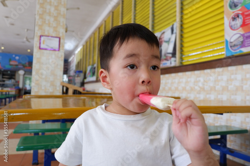 An Asian boy is wearing a white shirt eating ice cream.