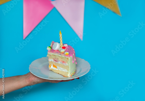Woman's hand holding a piece of birthday cake on blue background with copy space