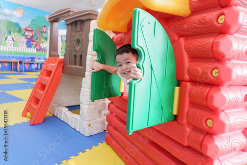An Asian boy wearing a white shirt is playing a toy house in the playground.