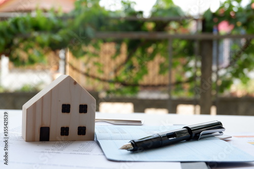 Model of house and pen placed on a bank book on table on blurred background