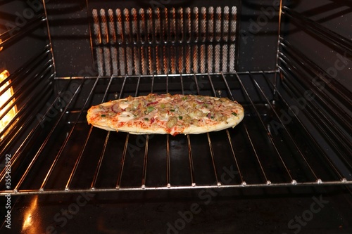 Bild auf Leinwand Oval shaped frozen tuna fish pizza baking on the rack in an electric oven