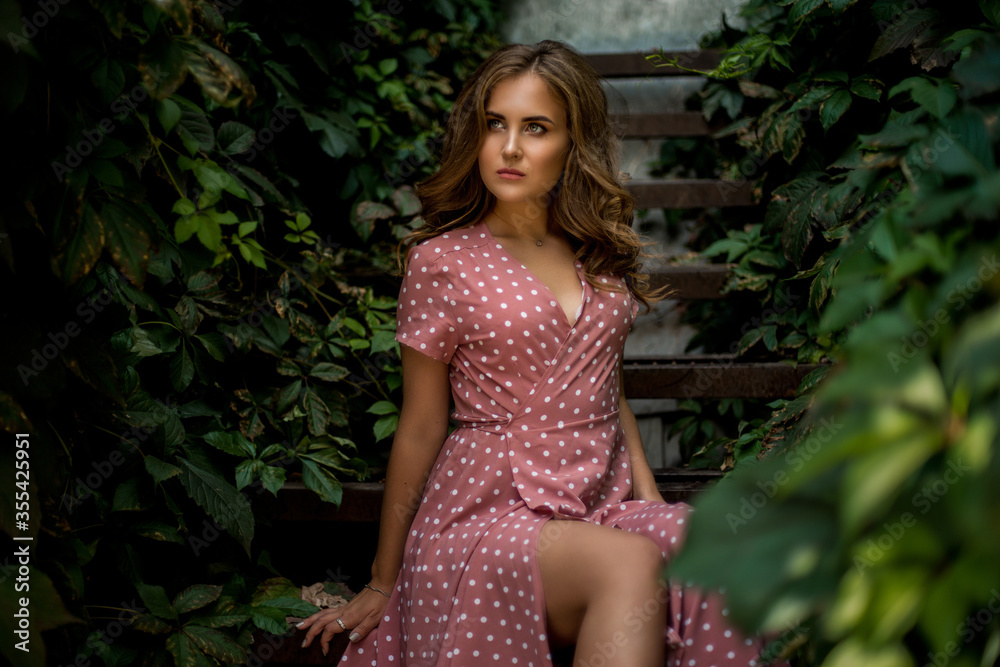 a very beautiful girl in a soft pink dress is sitting in the green ivy a very beautiful girl in a soft pink dress is sitting in the green ivy