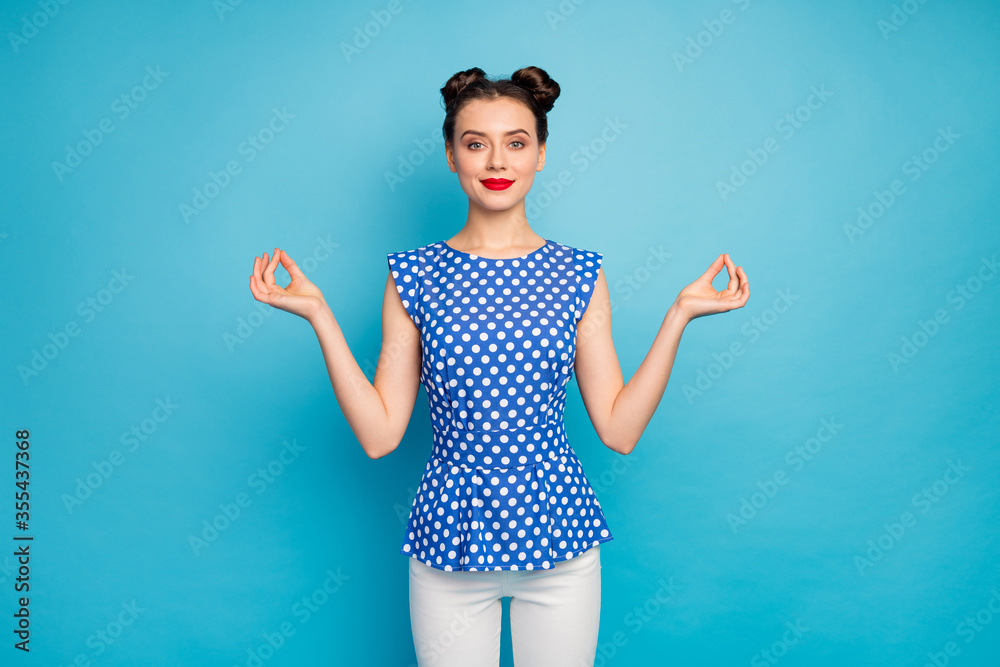 Fototapeta premium Zdjęcie całkiem pozytywnej pani trzymającej się za ręce palce asana postać medytująca czerpanie inspiracji relaks nosić bluzkę w kropki białe spodnie izolowane niebieskie tło