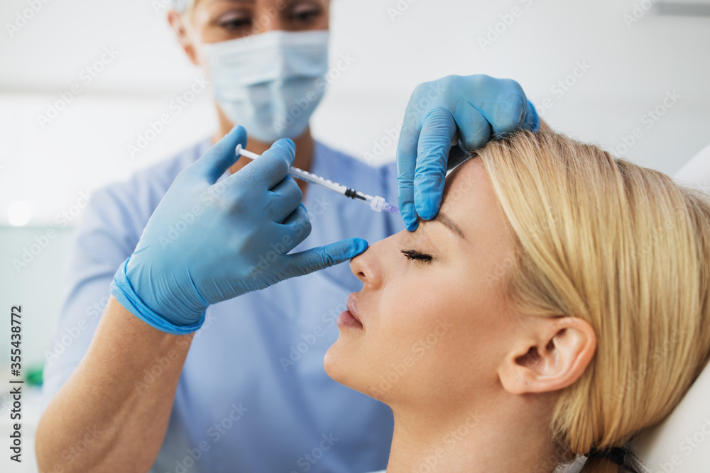 Attractive blond woman is getting a rejuvenating facial injections at beauty clinic. The expert beautician is filling female wrinkles by botulinum. Attractive blond woman is getting a rejuvenating facial injections at beauty clinic. The expert beautician is filling female wrinkles by botulinum.