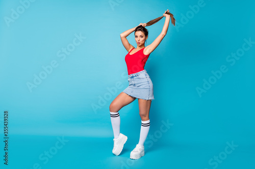 Fototapeta Naklejka Na Ścianę i Meble -  Full size photo of stunning chic girl send air kiss prepare for 14-february date hold hand make ponytail hairstyle wear red legs tank-top white singlet isolated over blue color background