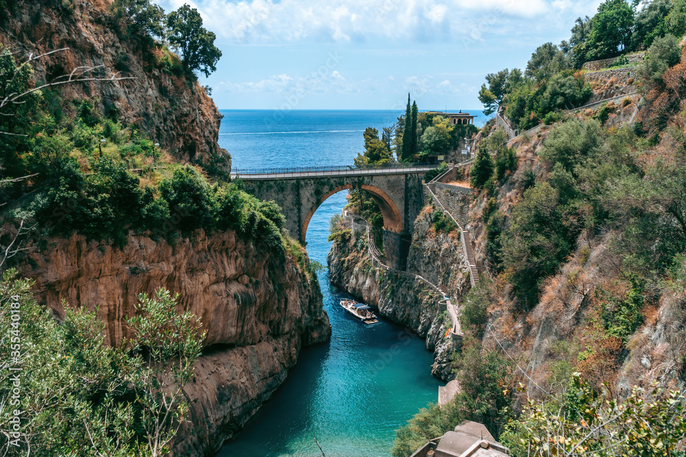 Architectural landmark, stone bridge. A view of the Fiordo of Furore in Amalfi coast, Travel and vacation concept. Summer day. motor boat, yacht with tourists for excursions. Italy.
