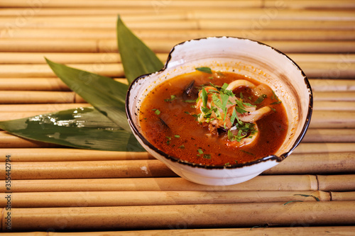 Close up view of Tom Yam soup in the white bowl served with bamboo leaves on the bamboo mat background. Appetizing and delicious seafood soup. Bouillabaisse soup. photo