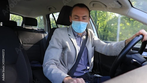 An adult business man driving his car wearing a face mask while entering the parking lot of his office