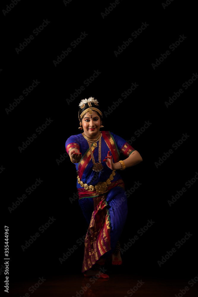 Bharatnatyam dancer performing in front of a dark background.
Bharatnatyam dancer performing in front of a dark background.