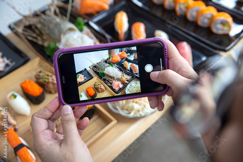 Woman photographing food served Japanese sushi set , Sushi nigiri rolls and sashimi in japanese food restaurant menu