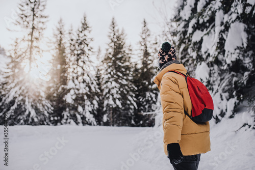 young man with yellow coat, red backpack and wool cap in a snowy mountain landscape