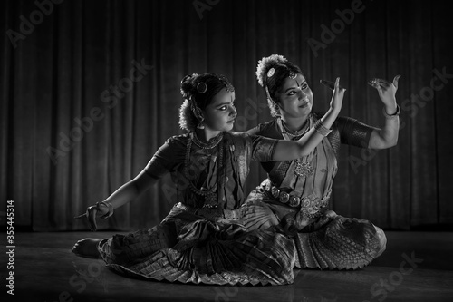 Black and white image of a bharatnatyam dancer teaching her young student.  
 photo