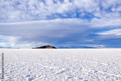 Landscape view salt marsh expanse with hexagonal salt formations, mountains in Salar de Uyuni, blue sky with textured clouds (Uyuni salt plain) during daytime, Bolivia. Nature Of South America