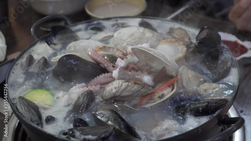 People eating Delicious Seafood Noodle Soup with shells and octopus Served In A Hot Pot At A Korean Restaurant In South Korea - close up photo