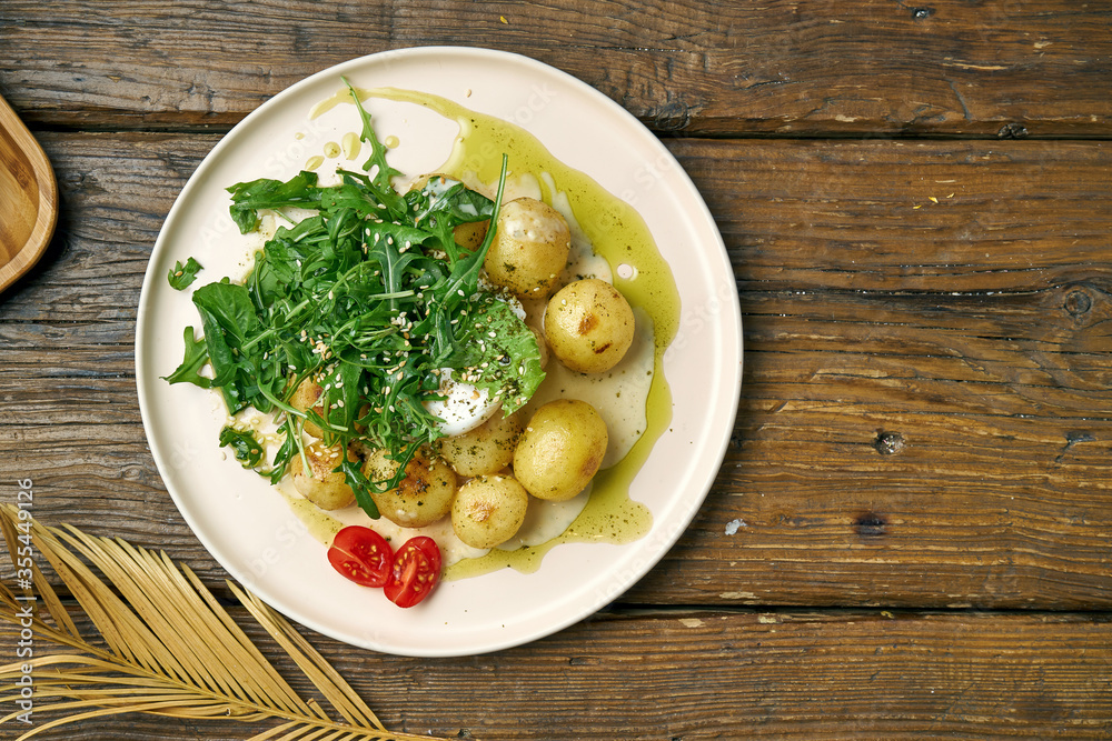 Boiled, young potatoes with arugula salad and poached egg seasoned with cream sauce on a wooden background