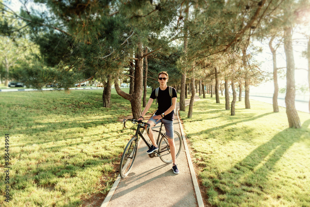 Young man standing with bicycle on path in summer park. Young man standing with bicycle on path in summer park.
