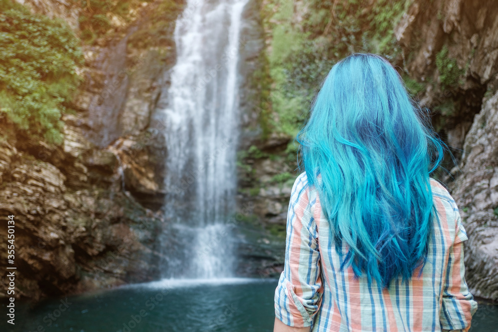 Rear view of woman with blue hair looking at waterfall.