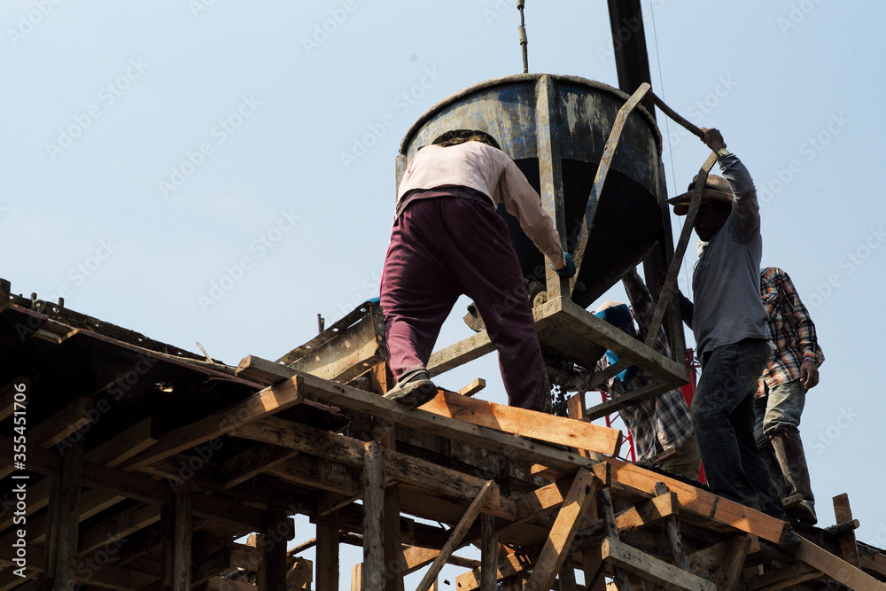 High angel view group of workers pouring the mixed cement from big steel bucket hanging from the crane. High angel view group of workers pouring the mixed cement from big steel bucket hanging from the crane.