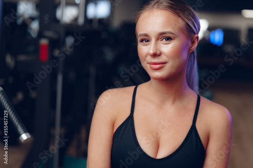 Close up portrait of a young blonde woman in sport bra in a dark gym © fotofabrika
