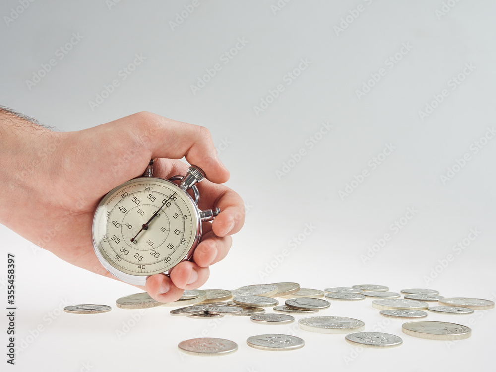 time is money. hand holding a stopwatch on a background of silver coins