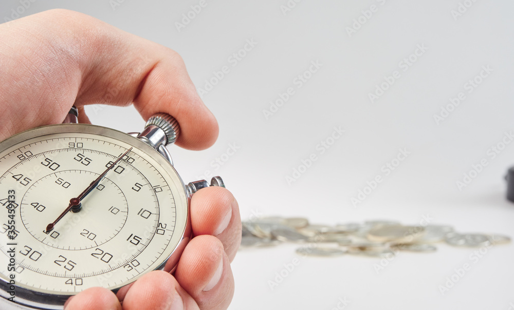 time is money. hand holding a stopwatch on a background of silver coins time is money. hand holding a stopwatch on a background of silver coins